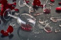 Two glasses of red wine, fallen and broken, lie on a glass table with glass fragments and petals of fresh red roses, under Royalty Free Stock Photo