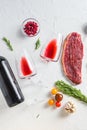 Two glasses of red wine near bottle and beef steaks over white concrete background, top view Royalty Free Stock Photo