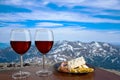 Two glasses of red wine with snacks assortment against mountain background. View of snowy peaks in the mountains