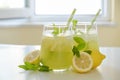 Two glasses of refreshing iced lemonade with lemon slices, mint leaves and ice on kitchen counter. Non alcoholic mojito drink on Royalty Free Stock Photo