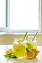 Two glasses of refreshing iced lemonade with lemon slices, mint leaves and ice on kitchen counter. Non alcoholic mojito drink on Royalty Free Stock Photo