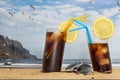 Two glasses of soda with ice and straws on the beach and sunglasses with blue sky and seagulls flying in Tenerife, Canary Islands Royalty Free Stock Photo