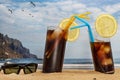 Two glasses of soda with ice and straws on the beach and and sunglasses with blue sky and seagulls flying in Tenerife, Canary Royalty Free Stock Photo