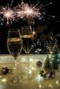 Two glasses of sparkling wine champagne with sparklers. Dark background with yellow light bokeh. Christmas tree toys on