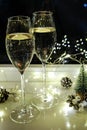 Two glasses of sparkling wine champagne with sparklers. Dark background with yellow light bokeh. Christmas tree toys on