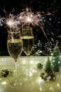 Two glasses of sparkling wine champagne with sparklers. Dark background with yellow light bokeh. Christmas tree toys on