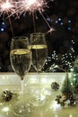 Two glasses of sparkling wine champagne with sparklers. Dark background with yellow light bokeh. Christmas tree toys on the table