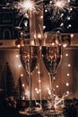 Two glasses of sparkling wine champagne with sparklers. Dark background with yellow light bokeh. Christmas tree toys on the table