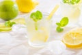 Two glasses with summer drink mojito with lime, lemon and mint, with ice cubes on white wooden background