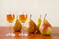 Two glasses of traditional bulgarian home made fruit brandy krushova rakia and four pears on a wooden table against light beige