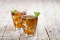 Two glasses with traditional iced tea with lemon, mint leaves and ice cubes in glass on rustic wooden table background