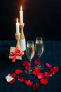 Two glasses with white champagne, gift box and petals of red roses on the background of candles Royalty Free Stock Photo