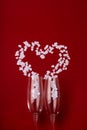 Two glasses with white hearts and splashing in heart shape on red background. Valentine's Day, love concept. Vertical Royalty Free Stock Photo