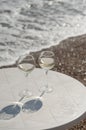 Two glasses of white wine on a table by the ocean. Sparkling bokeh of pebbles on the shore. The atmosphere of summer holidays Royalty Free Stock Photo