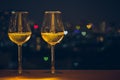 Two glasses of white wine on wooden table of rooftop bar with colorful love shape bokeh of city light and space for text