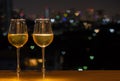 Two glasses of white wine on wooden table of rooftop bar with colorful love shape bokeh of city light and space for text