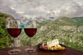 Two glasses of wine with charcuterie assortment on view of mountains with clouds in Croatia. Glass of red wine with different