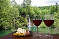 Two glasses of wine with charcuterie assortment waterfall background in Croatia. Glass of red wine with different snacks - plate