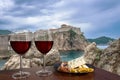 Two glasses of wine with cheese and meat assortment on view of the fortress walls, rocky coast and blue sea in Dubrovnik, Croatia Royalty Free Stock Photo