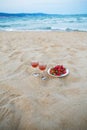 Two glasses of wine and a plate of strawberries on a sandy beach, a picnic near the sea Royalty Free Stock Photo