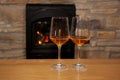 Two glasses of wine standing on a table in front of a fireplace in which firewood burns with a bright flame, a concept of a Royalty Free Stock Photo