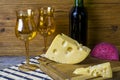 Two glasses with wine, yellow and red cheese on a cutting board, a bottle of wine stands on a wooden background