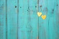 Two gold hearts hanging on antique teal blue wood fence