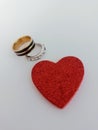 Two gold and silver wedding rings beside a red heart on a white background Royalty Free Stock Photo