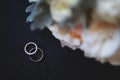 Two gold wedding rings with a diamond on a black background with a wedding bouquet Royalty Free Stock Photo