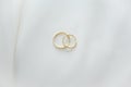 Two gold wedding rings placed together on a white textile surface with copy space.