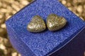 Two golden heart with glitter on a small blue gift box on golden foil background. Valentine present. Special occasion