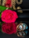 Two golden wedding rings in focus on blue gem stone and red rose out of focus on a dark reflective surface. Concept love, romance Royalty Free Stock Photo