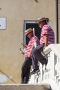Two gondoliers in traditional costumes on the bridge during a rest break, Venice, Italy