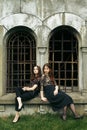 Two gorgeous women in black sitting at old church in the city and posing, stylish gothic themed, ladies party