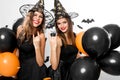 Two gorgious women in black dresses and witch hats hold black and orange balloons. Halloween