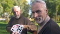 Two grandfathers playing cards on bench in park, weekend leisure, old age hobby