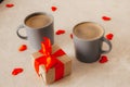 Two gray coffee cups sit on the table, next to a gift box with a red bow and scattered red confetti hearts. The concept of St. Royalty Free Stock Photo