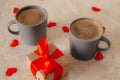 Two gray coffee cups sit on the table, next to a gift box with a red bow and scattered red confetti hearts. The concept of St. Royalty Free Stock Photo