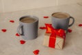 Two gray coffee cups sit on the table, next to a gift box with a red bow and scattered red confetti hearts. The concept of St. Royalty Free Stock Photo