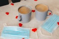 Two gray cups of coffee are on the table, along with medical masks and red confetti hearts scattered around. The concept of St. Royalty Free Stock Photo