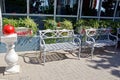 Two gray metal benches on the sidewalk against the wall with windows and flowerpots with plants and flowers