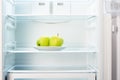 Two green apples on white plate in open empty refrigerator Royalty Free Stock Photo