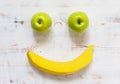 Two green apples and a yellow banana in the form of a smile on a white wooden background Royalty Free Stock Photo