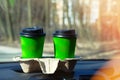 Two green paper cups with tea or coffee for a couple in car on sunny blurred background. Takeaway, social media. Morning breakfast Royalty Free Stock Photo