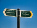 Two green signs on a grey metal post point the directions of the England Coast Path and Saxon Shore Way.