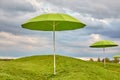 Two green sunny umbrellas on green grass against a cloudy sky. Umbrellas among the hills. Protection concept. Royalty Free Stock Photo