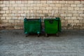 Two Green Trash Dumpsters In Front Of White Brick Wall Front View With Room For Text. Two metal dumpster cans on the side of the s