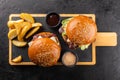 Two grilled hamburgers and fries on a wooden board, ready to eat. Royalty Free Stock Photo