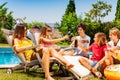 Group of kids drink soda on deck chairs by pool