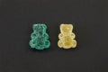 Two gummy bears in sugar, yellow and blue, on black background.